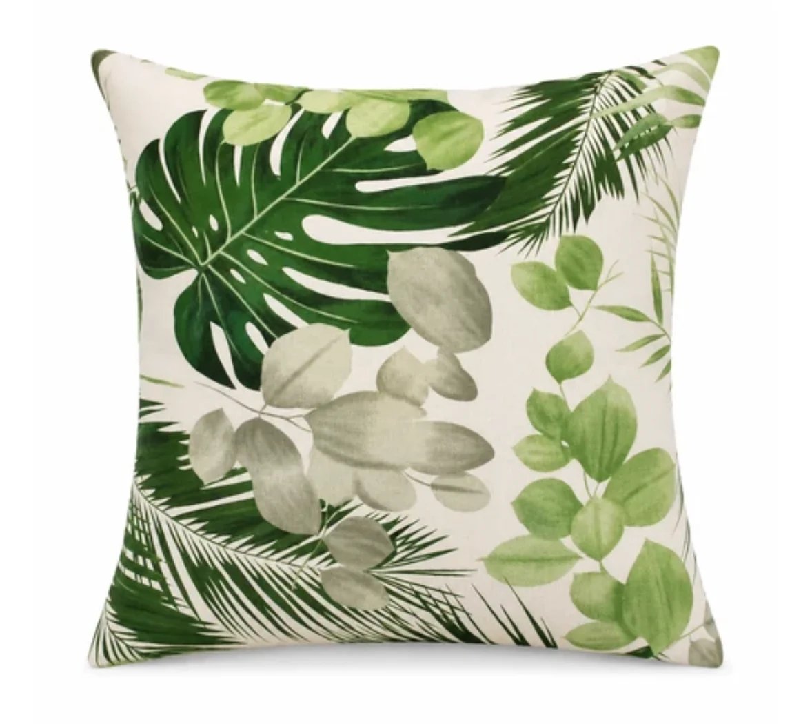 Cream throw pillow with botanical print featuring green monstera leaves, palm fronds, and eucalyptus leaf designs