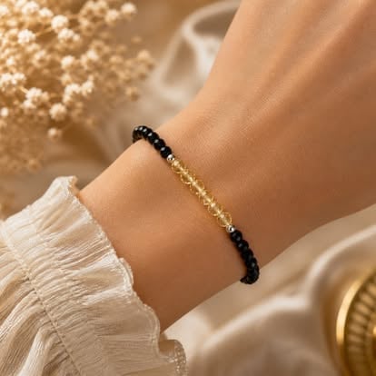 Black beaded bracelet with gold chain accents worn on wrist with white lace sleeve and gold jewelry in background